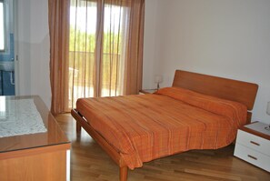 A bedroom with a wooden bed, a bedside table, a nightstand, and a window with curtains.