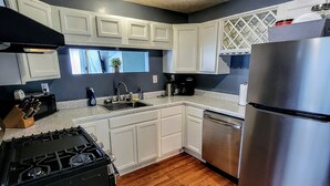 A modern kitchen with white cabinets, a stainless steel refrigerator, a dishwasher, a stove, and a sink.