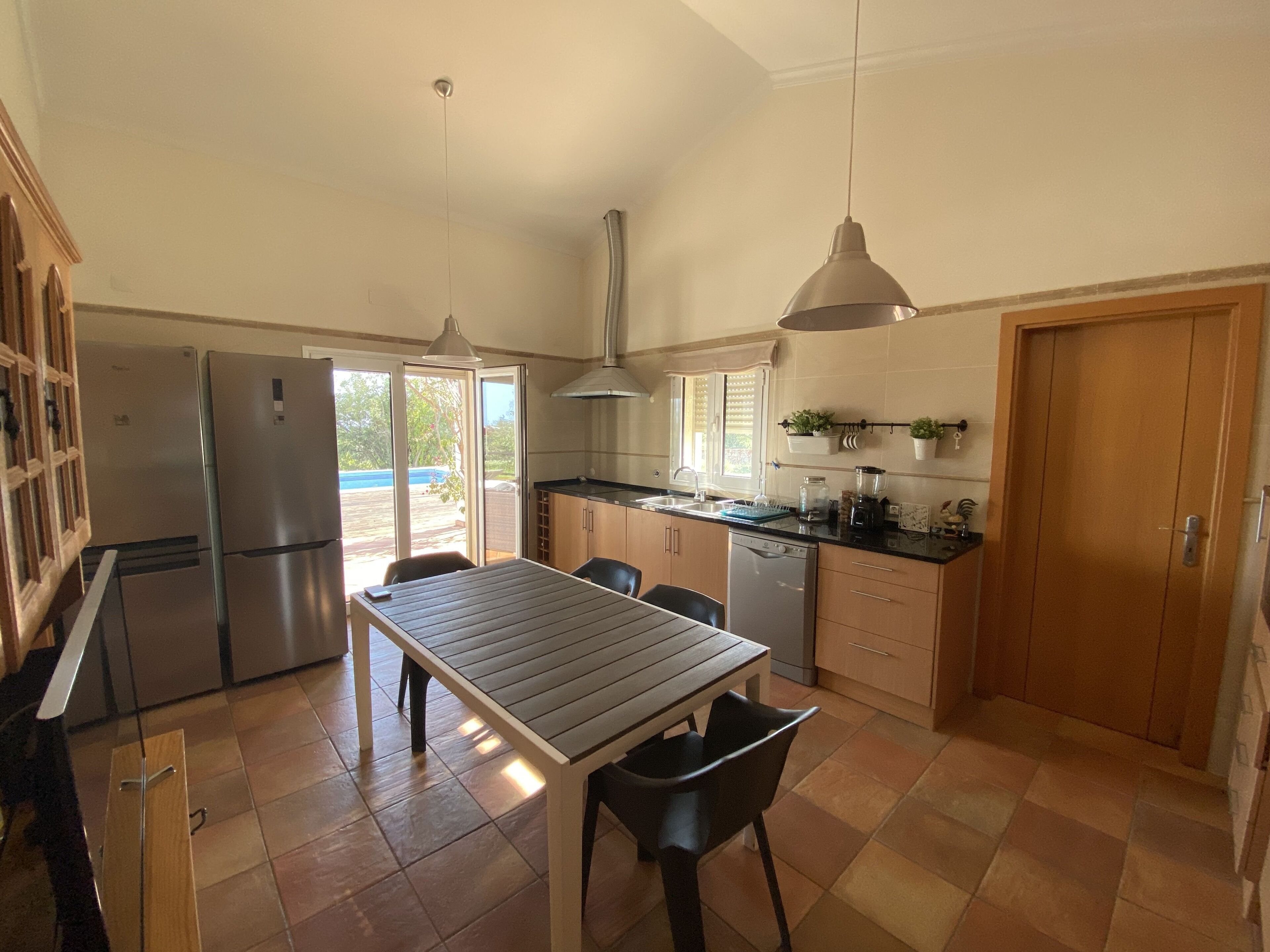 Une cuisine compacte comprenant une table à manger, des chaises, un réfrigérateur, un lave-vaisselle et des luminaires suspendus.