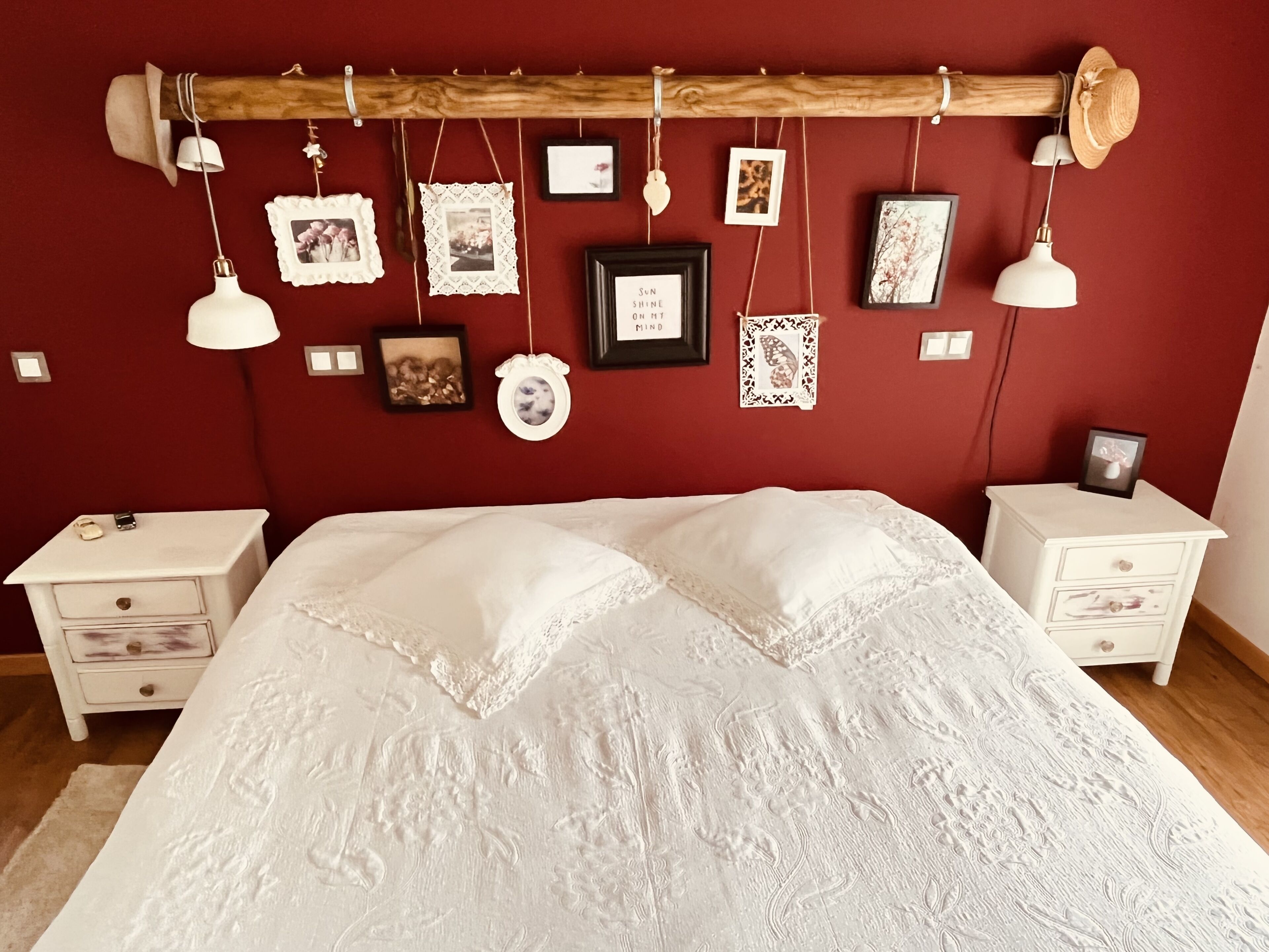 A bedroom with a wooden headboard, white bedding, and multiple framed pictures on the wall.