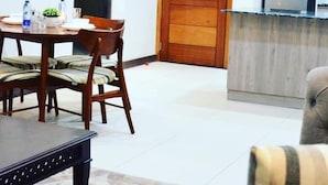 Un coin repas avec une table et des chaises, une porte en bois et un espace cuisine comprenant des placards et un réfrigérateur.