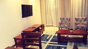 Un salon avec un téléviseur fixé au mur, deux fauteuils à motifs, une table basse et une table à manger avec des chaises.