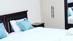 Un lit bien fait, avec du linge de lit blanc et une serviette enroulée, une tête de lit en bois foncé et une petite table de chevet avec une lampe.