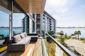 A modern balcony with a sofa, glass railings, and a view of the sea and city skyline. - DHH Bluewater Island Building 2 Sea View (Dubai)