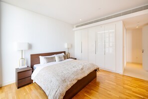 A modern bedroom with a wooden bed, white walls, and a large wardrobe. - DHH Bluewater Island Building 2 Sea View (Dubai)