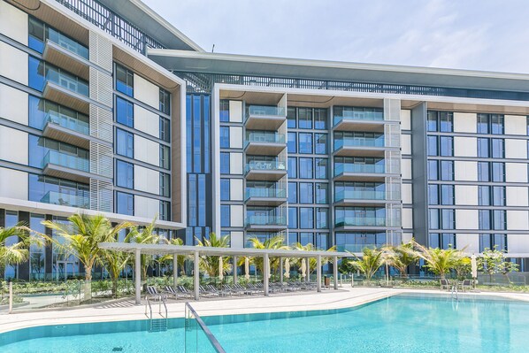 A modern hotel with a pool area, featuring multiple balconies, a covered seating area, and lush landscaping. - DHH Bluewater Island Building 2 Sea View (Dubai)