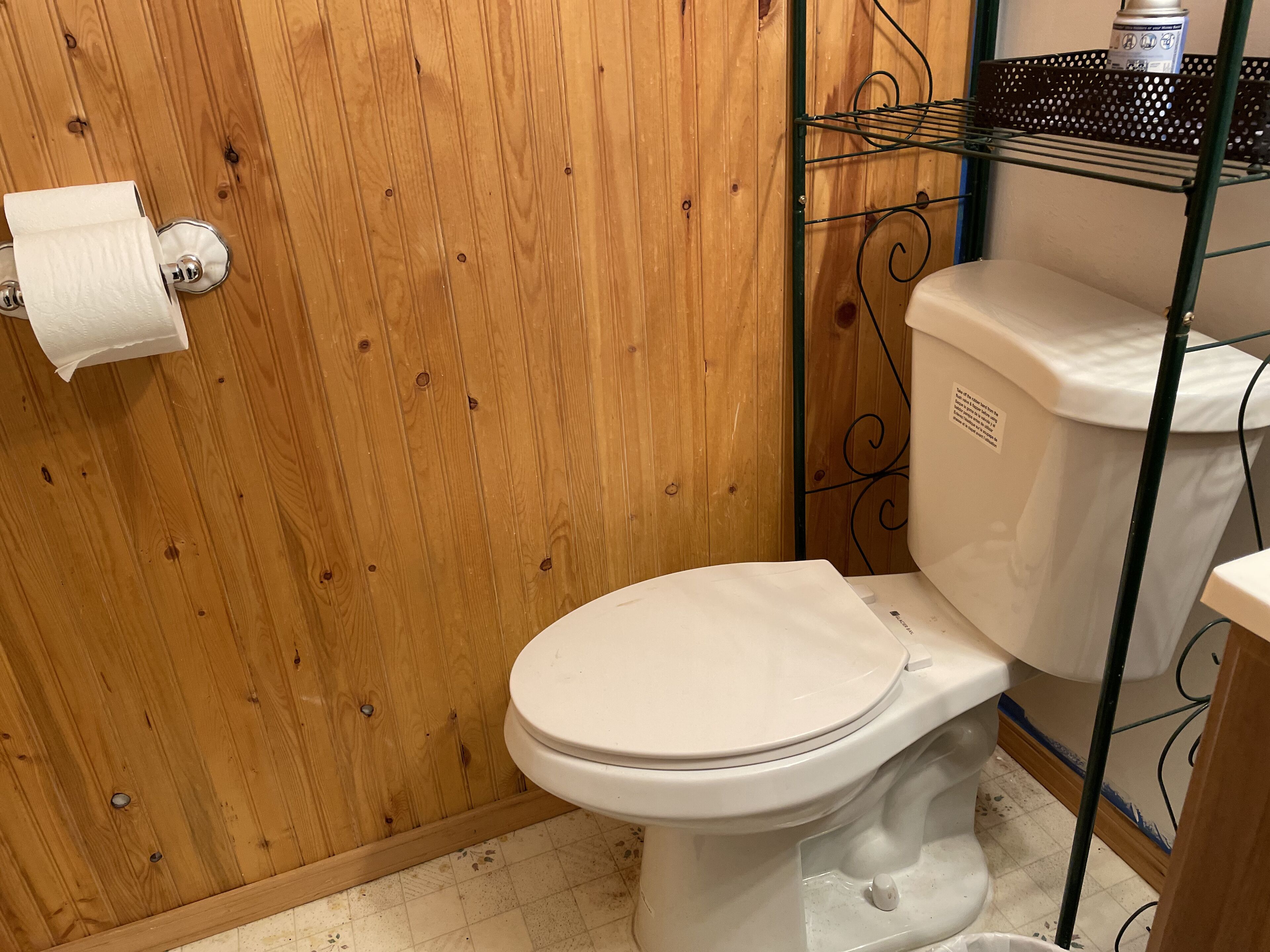 A bathroom with a wooden wall, a toilet, and a metal rack with a canister.