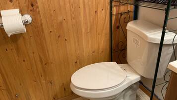 A bathroom with a wooden wall, a toilet, and a metal rack with a canister.