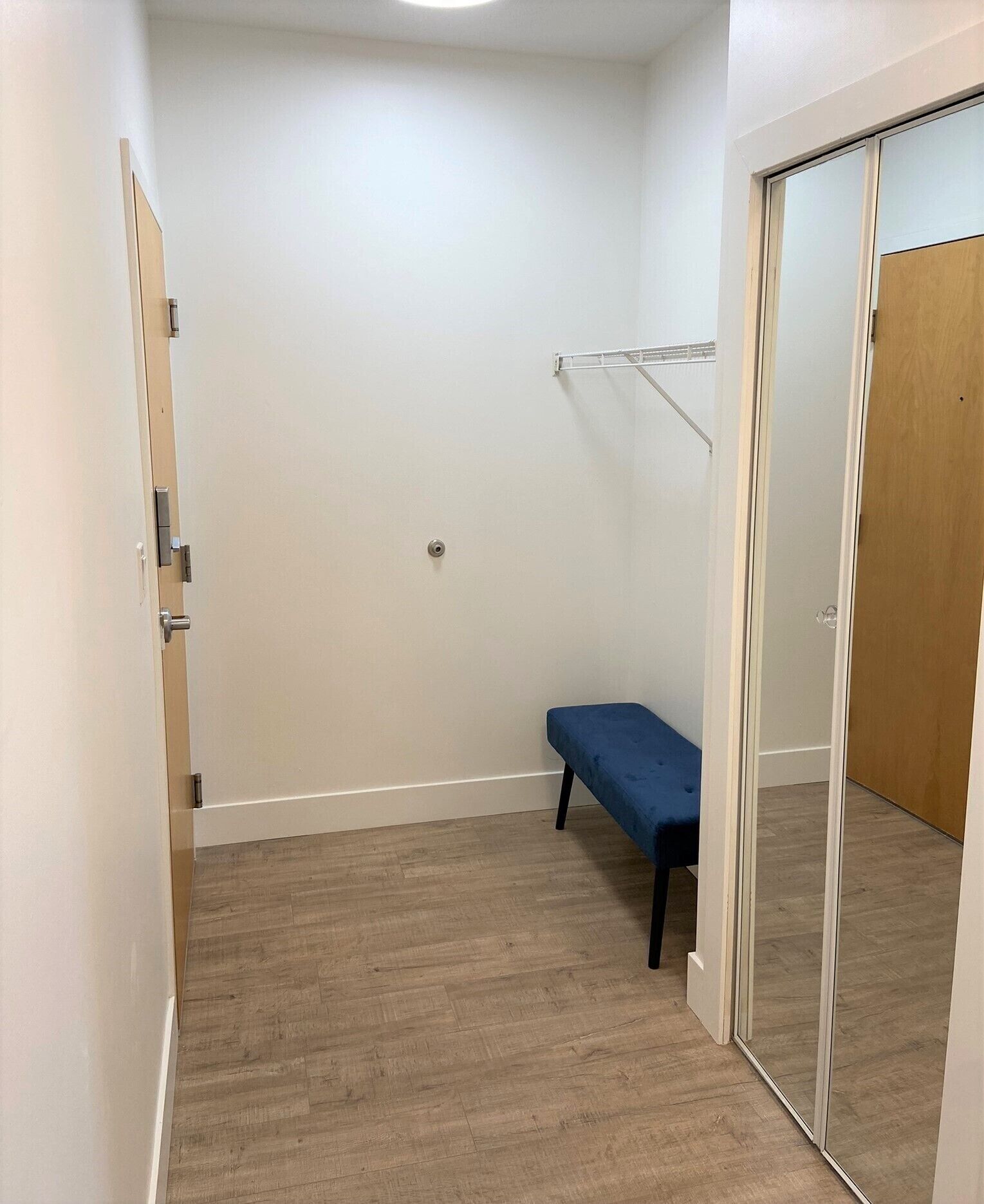 Una habitación pequeña y estrecha con un banco de madera, una estantería de metal y una puerta corredera.