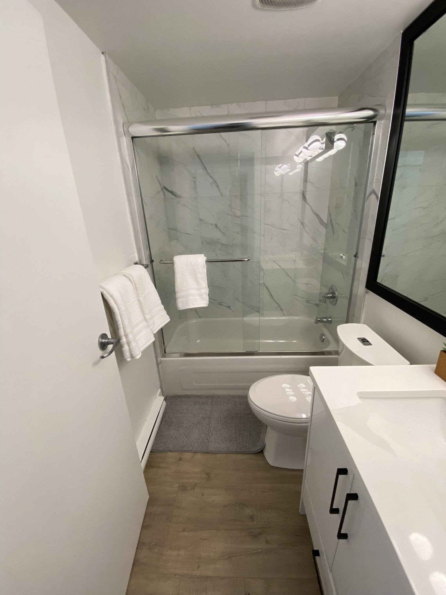Un baño moderno con cabina de ducha de vidrio, inodoro blanco y tocador con espejo.