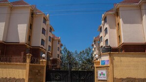 Un complejo residencial amurallado con varios edificios de apartamentos, cielo despejado y un cartel que indica un sistema de seguridad.