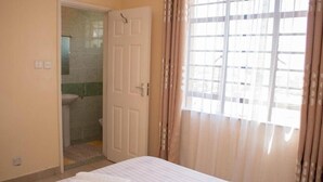Un dormitorio con cama, un baño con inodoro y lavamanos, y una ventana con cortinas.