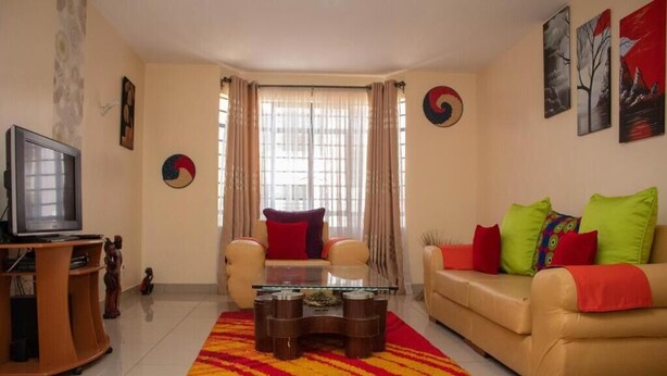 Una sala de estar con sofá, una mesa de centro, televisor y una ventana con cortinas.