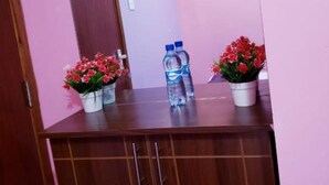 A room with a wooden vanity, two potted red flowers, a water bottle, and a mirror reflecting the room. - Stay.Plus Karibu Homes Apartment (Athi River)