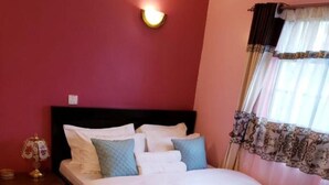 A bedroom with a bed, a nightstand, a lamp, and a window with curtains. - Stay.Plus Karibu Homes Apartment (Athi River)