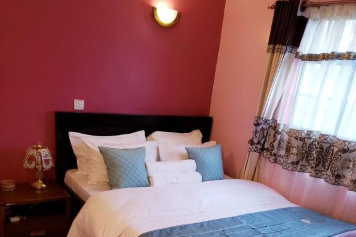Een slaapkamer met een bed, nachtkastje, lamp en raam met gordijnen.