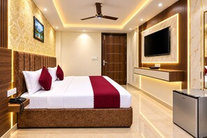A hotel room with a large bed, a television mounted on the wall, a ceiling fan, and a minibar. - Delhi Vista by Kelvish Hotel (New Delhi)