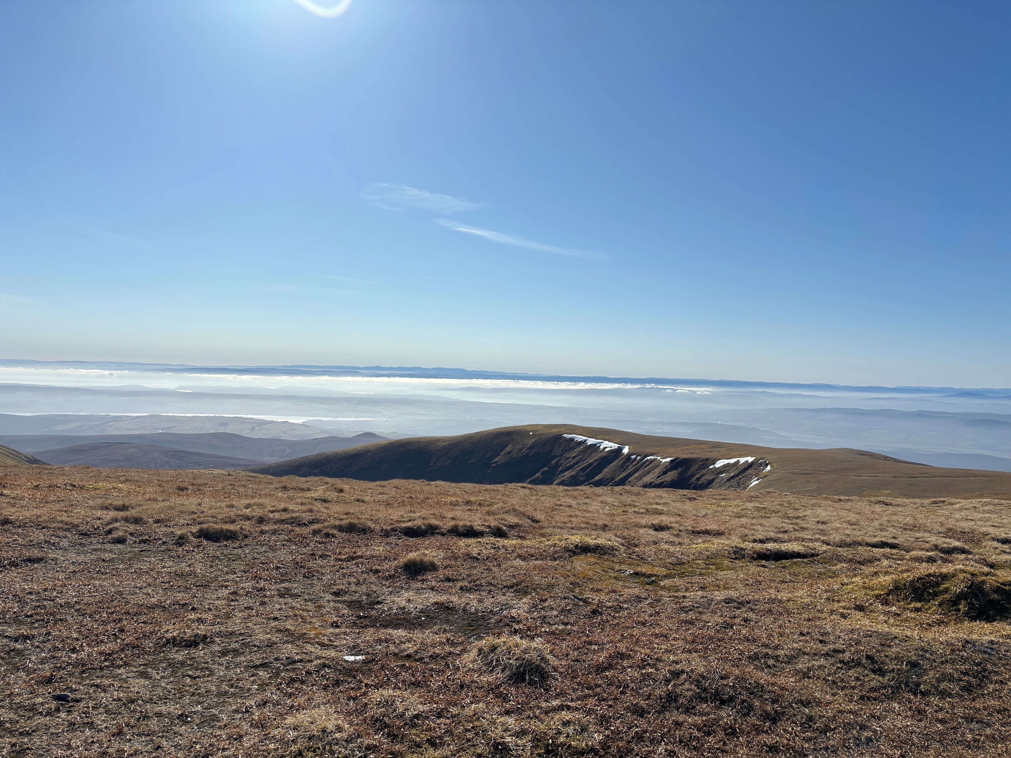 Et panorama over et bjerglandskab med klar himmel og fjernt hav.