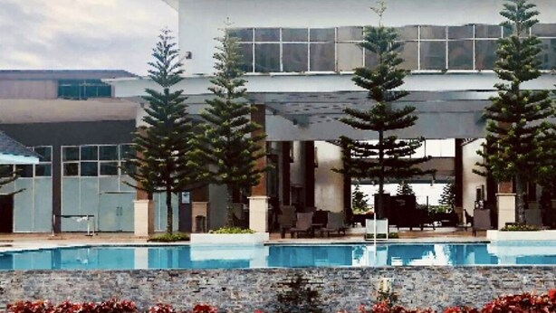 A modern building with a swimming pool, surrounded by trees and red flowers. - Tagaytay Garden View Suites (Tagaytay)