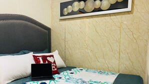 A neatly made bed with a laptop, a decorative pillow, and a framed artwork on the wall. - Tagaytay Garden View Suites (Tagaytay)