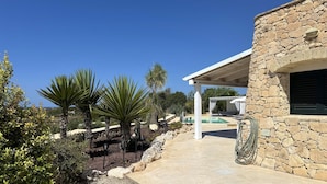 A stone building with a covered patio area, a pool, and surrounding vegetation.