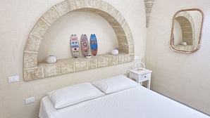 A bedroom with a bed, a shelf with surfboards, a mirror, and a small table.