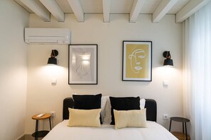 A hotel room with a bed, two bedside tables, a wall-mounted air conditioner, and two wall-mounted lamps.