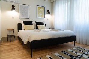 Ein Schlafzimmer mit schwarzem Metallbettgestell, weißer Bettwäsche, zwei Wandleuchten und einem gemusterten Teppich.