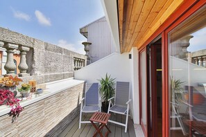 A balcony with a wooden floor, white walls, and a glass door leading inside. There are two white chairs and a small table with a potted plant. - TOMAS LOFT - Charming loft located in downtown Porto (Porto)