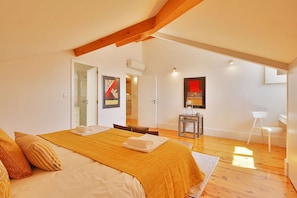 A bedroom with a bed, a wooden floor, a white chair, and a door leading to a bathroom. - TOMAS LOFT - Charming loft located in downtown Porto (Porto)