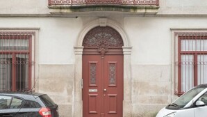 Ein Gebäude mit einer roter Tür, zwei Fenstern mit Metallgittern und einem Balkon mit schmiedeeisernem Geländer.