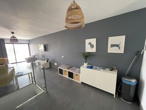 A modern living room with a grey wall, a white sofa, a glass coffee table, a wicker hanging light, and framed artwork.