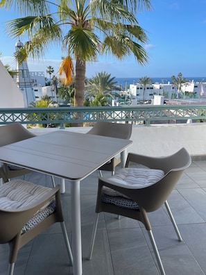 An outdoor patio with a table and chairs, overlooking a cityscape and the sea.
