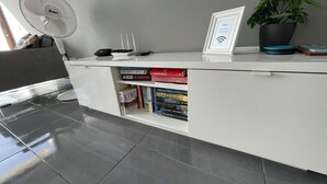 Uma mesa de escritório moderna com tampo branco, um ventilador vertical, um laptop, um sinal de Wi-Fi emoldurado e um vaso de planta.