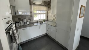 Uma cozinha moderna com armários brancos, pia de aço inoxidável e janela com cortinas estampadas.