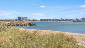 A coastal view with a sandy beach, a rocky breakwater, and a row of houses in the background. - Giggles Beach House in Silver Sands (Silver Sands)