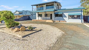 A two-story house with a covered patio area and a gravel driveway. - Giggles Beach House in Silver Sands (Silver Sands)