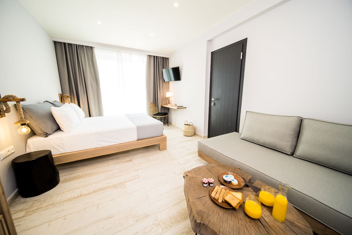 A modern hotel room with a bed, sofa, and breakfast table with pastries and juice.