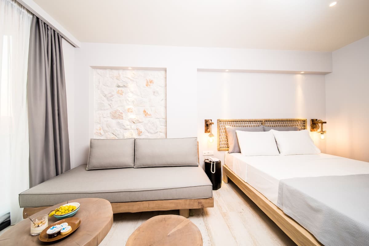 A modern hotel room with a sofa, a bed, a small table with a bowl of fruit, and a decorative wall piece.