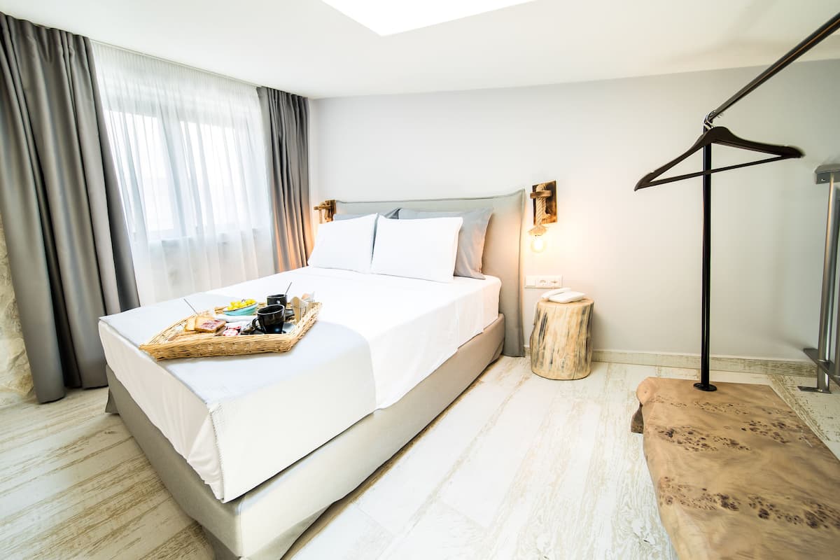 A neatly made bed with a tray of breakfast items, a bedside table with a lamp, and a wooden bench.