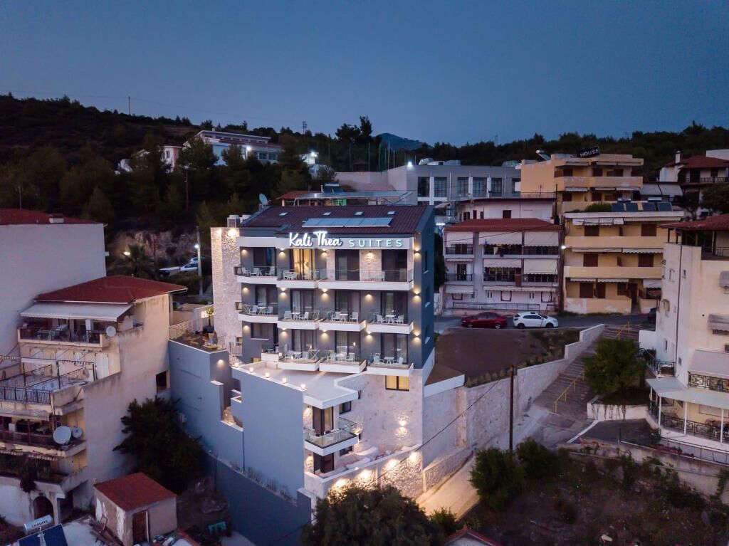 Un hôtel à plusieurs étages, nommé « Kali Thea Suites », doté de balcons et d’espaces extérieurs aménagés pour s’asseoir.