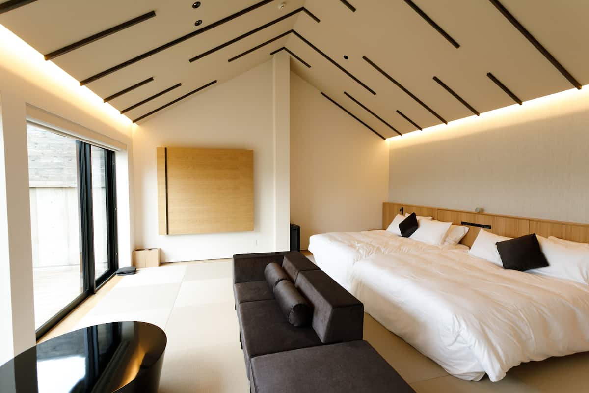 Una habitación de hotel moderna con una cama grande, un sofá y vistas de la ciudad a través de amplios ventanales.