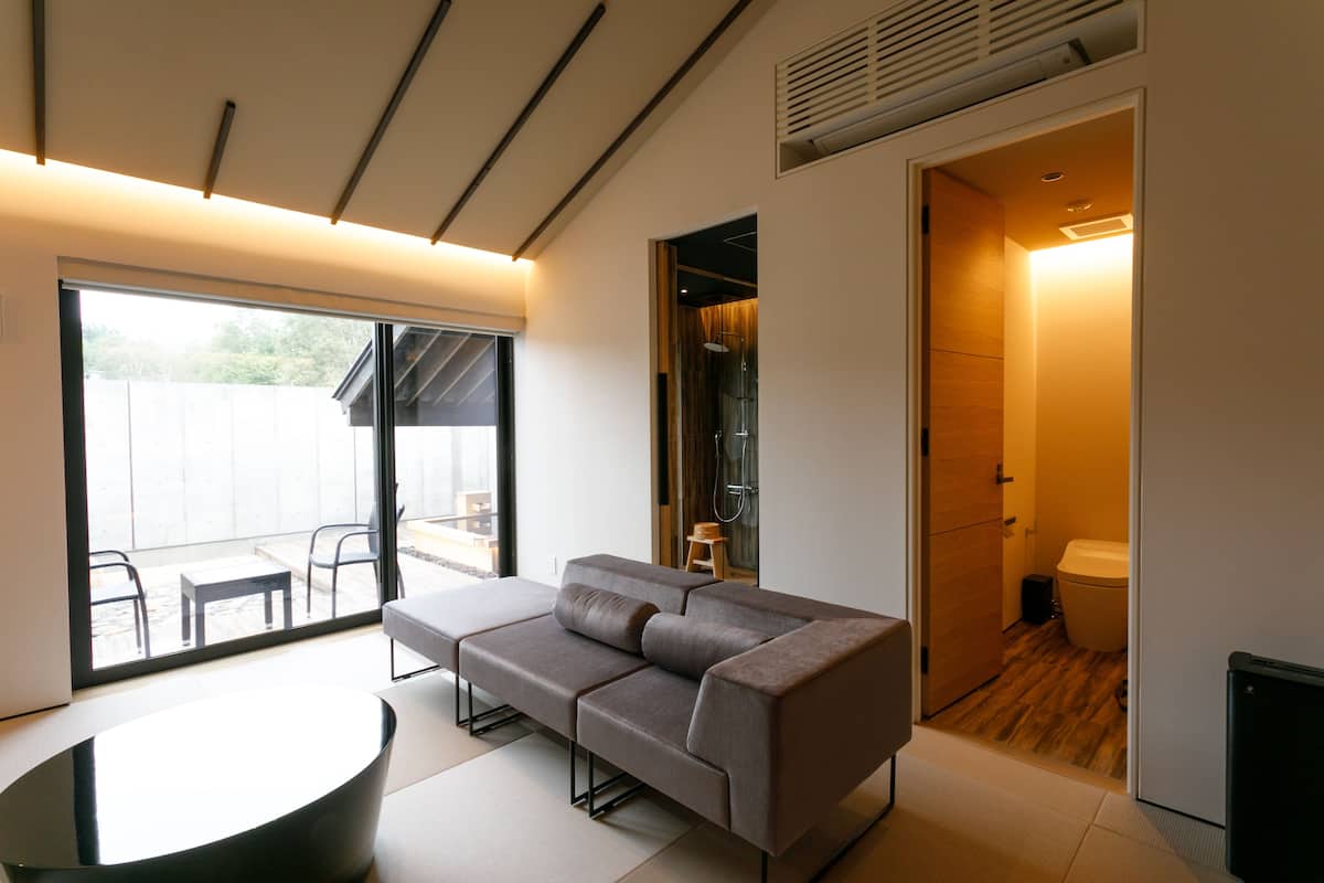 Una sala de estar moderna con un sofá, una mesa de comedor y un ventanal corredero que da a un patio exterior.
