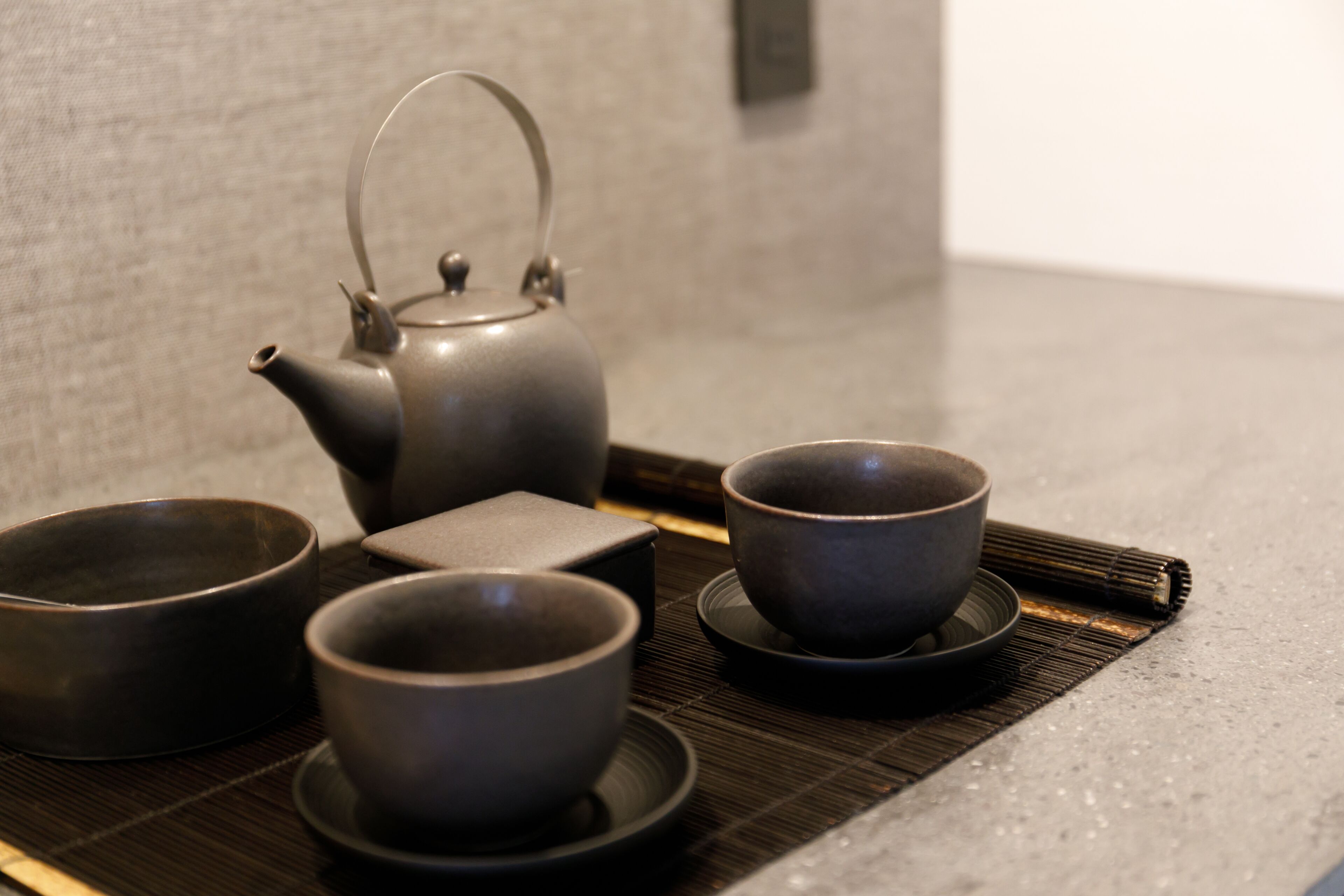 A tea set with a teapot and three cups on a bamboo mat.