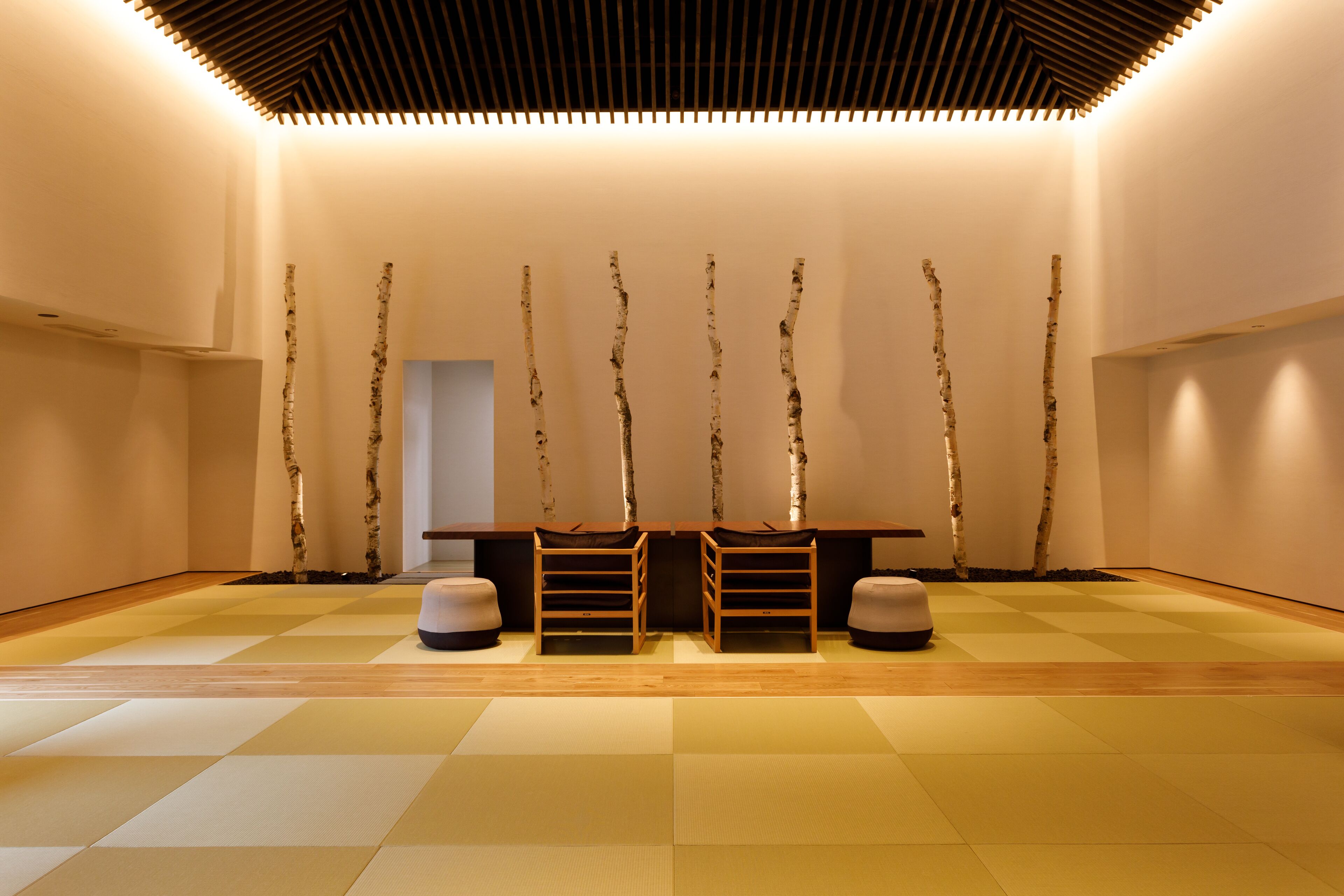 A minimalist room with a wooden floor, a central table, and birch tree sculptures on the wall.