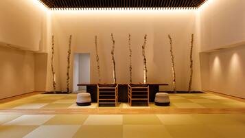 A minimalist room with a wooden floor, a central table, and birch tree sculptures on the wall.