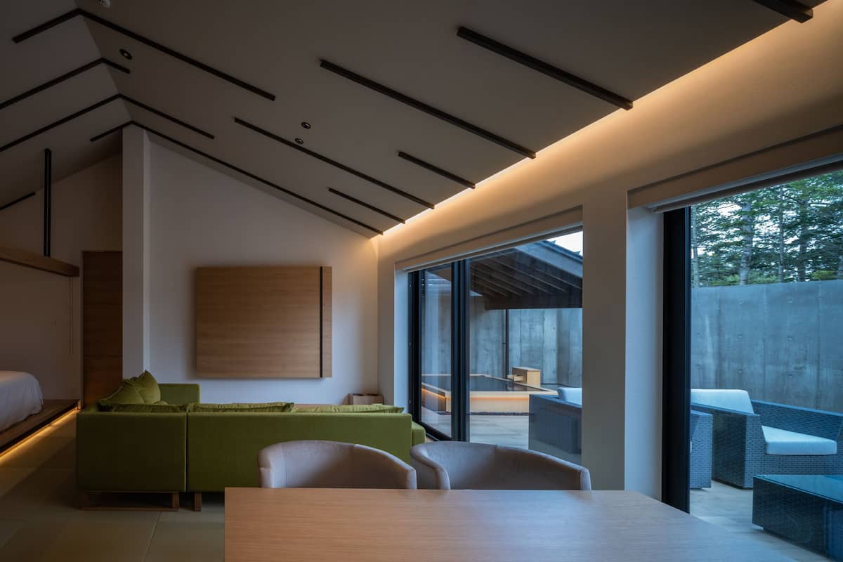 Un interior moderno con cama, sofá, comedor, ventanas amplias y vistas al exterior.