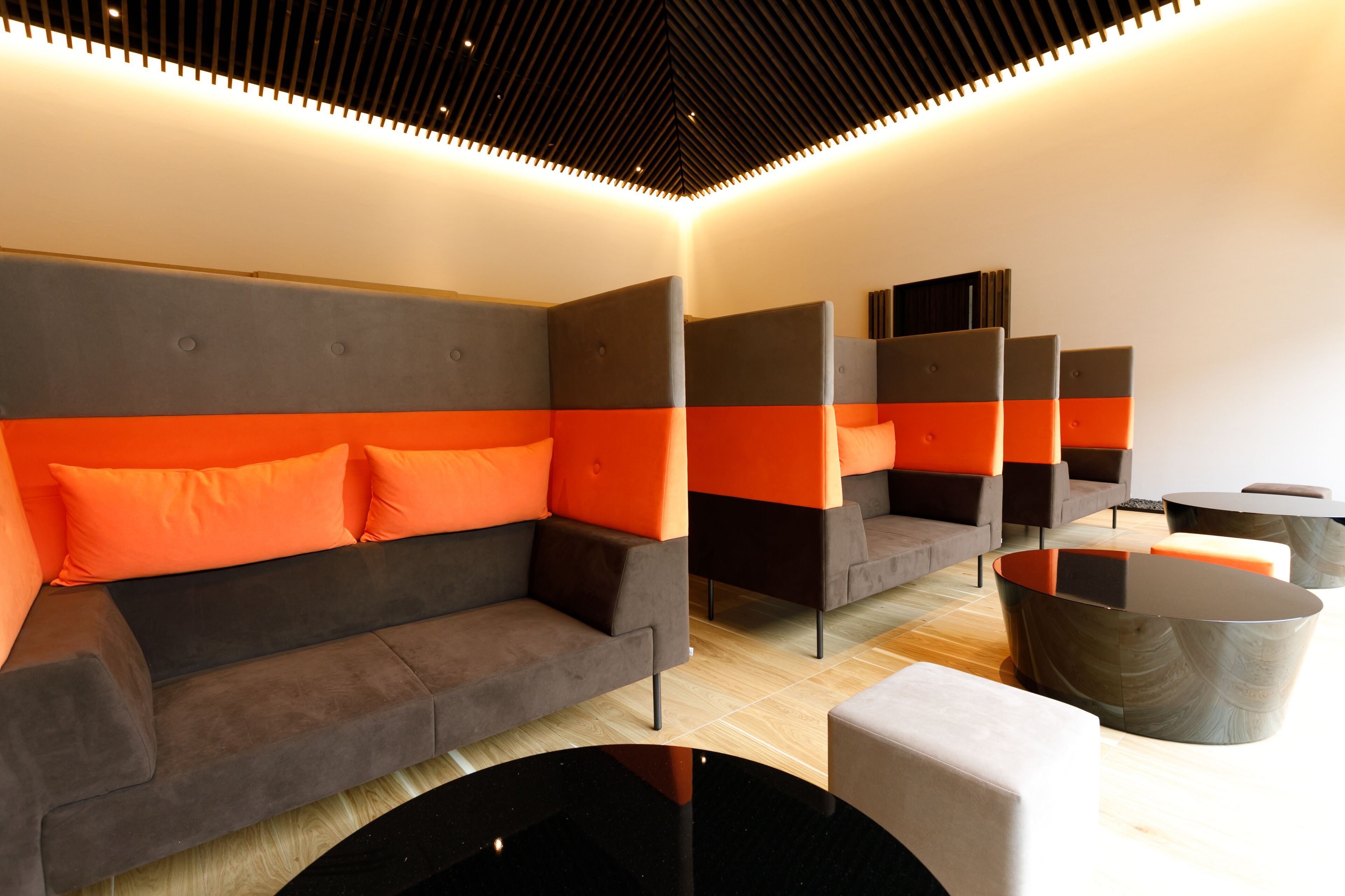 A modern lounge area with sofas and tables, featuring a geometric ceiling design and a wooden floor.