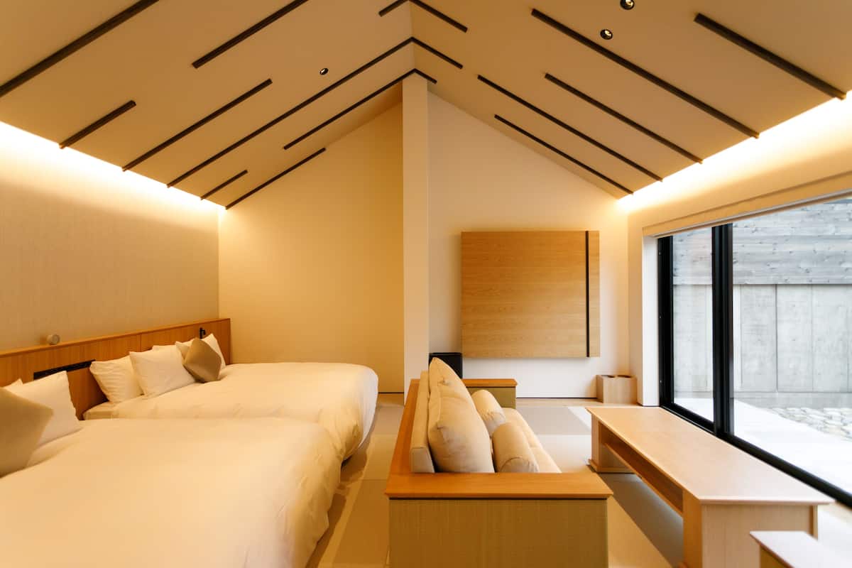 Una habitación de hotel moderna con una cama grande, un sofá, un escritorio y un ventanal amplio.