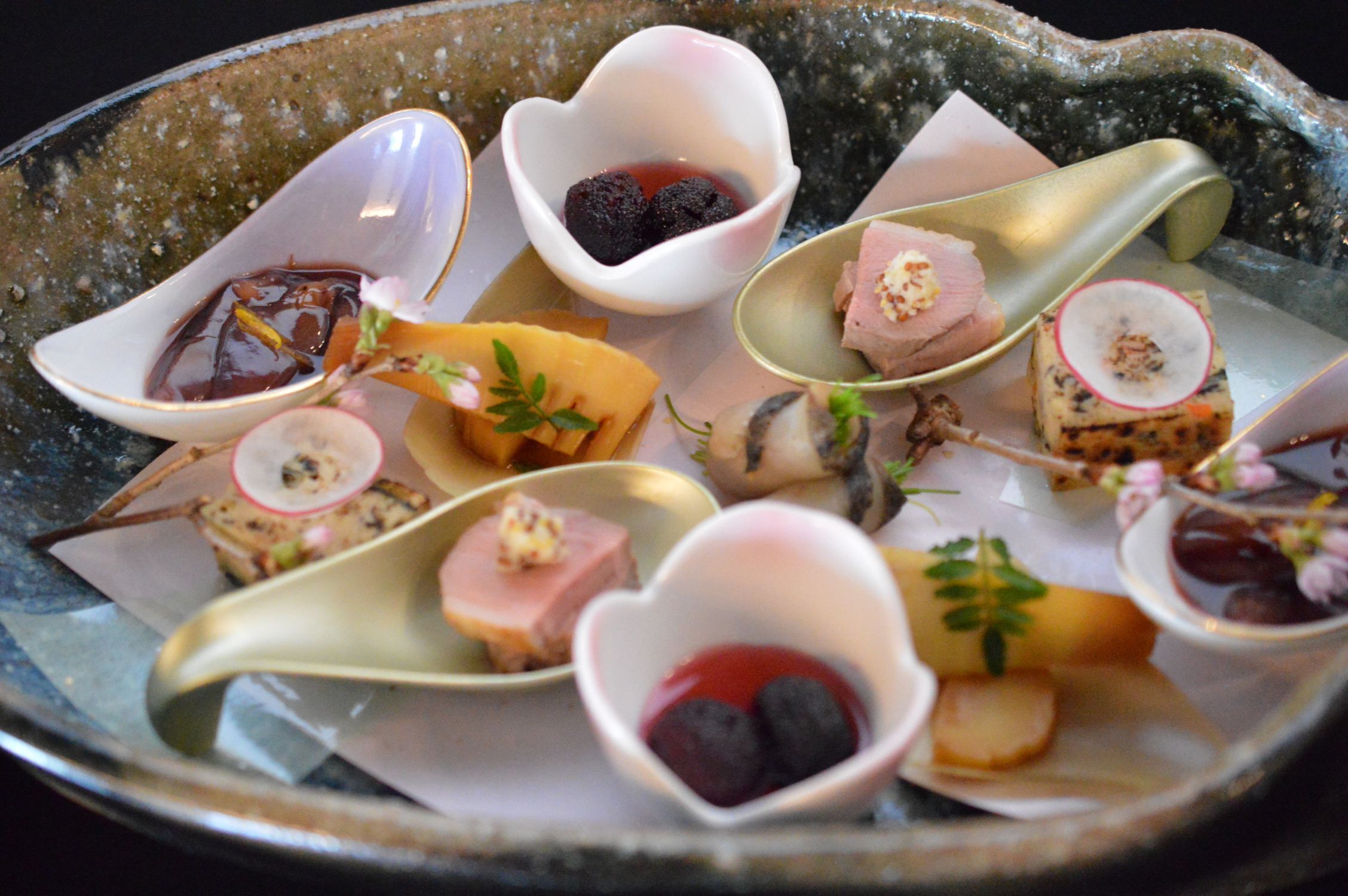 A variety of small, heart-shaped dishes with different food items and garnishes on a ceramic plate.